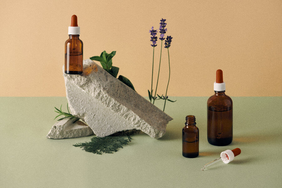 Pipetten und Ölfläschchen auf einem Naturstein arrangiert mit Lavendel, Minze und Rosmarin in warmen Cremetönen.